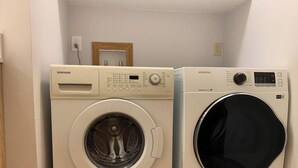 Two front-loading washing machines in a laundry room with a wooden door and a power outlet on the wall. - Cozy bedroom close to C-train (Calgary)