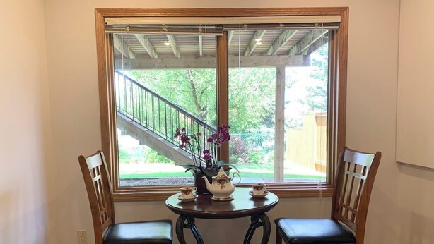 A dining area with a table and two chairs, a window with a view of a staircase and greenery, and a decorative vase with flowers. - Cozy bedroom close to C-train (Calgary)