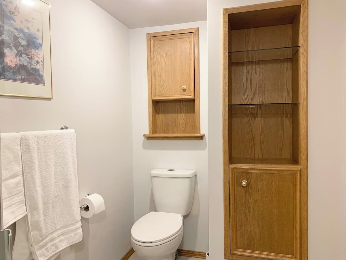 A bathroom with a toilet, a wooden cabinet above the toilet, and a towel rack with a towel.
