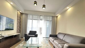 A modern living room with a glass coffee table, leather sofa, and a flat-screen TV mounted on the wall. - Lux Suites Siaya Park Apartments (Nairobi)