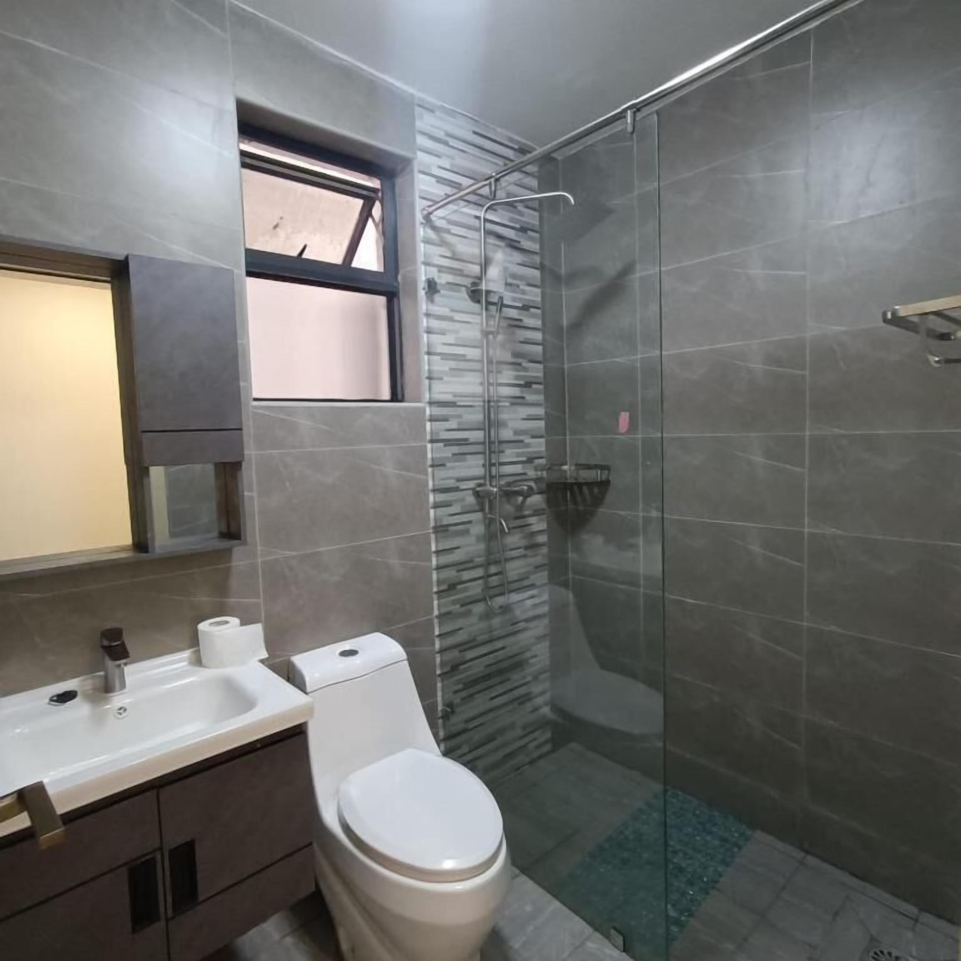 Une salle de bain moderne avec une douche à l’italienne en verre, des toilettes et un lavabo avec un miroir au-dessus.