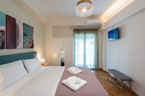 A hotel room with a bed, a bench, a TV, and artwork on the wall. - Blue Ark Wanderlust (Athens)