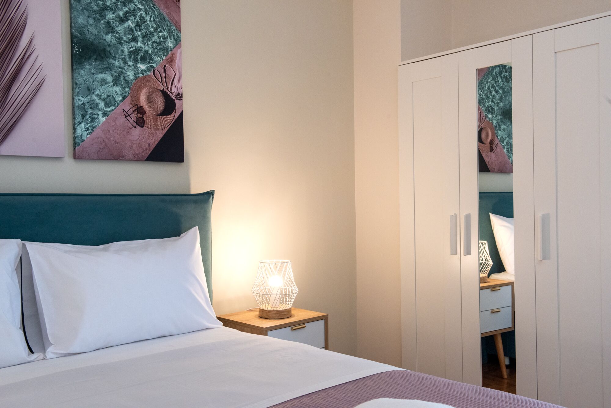 A neatly made bed with white linens, a bedside lamp, and a wall-mounted mirror reflecting part of the room.