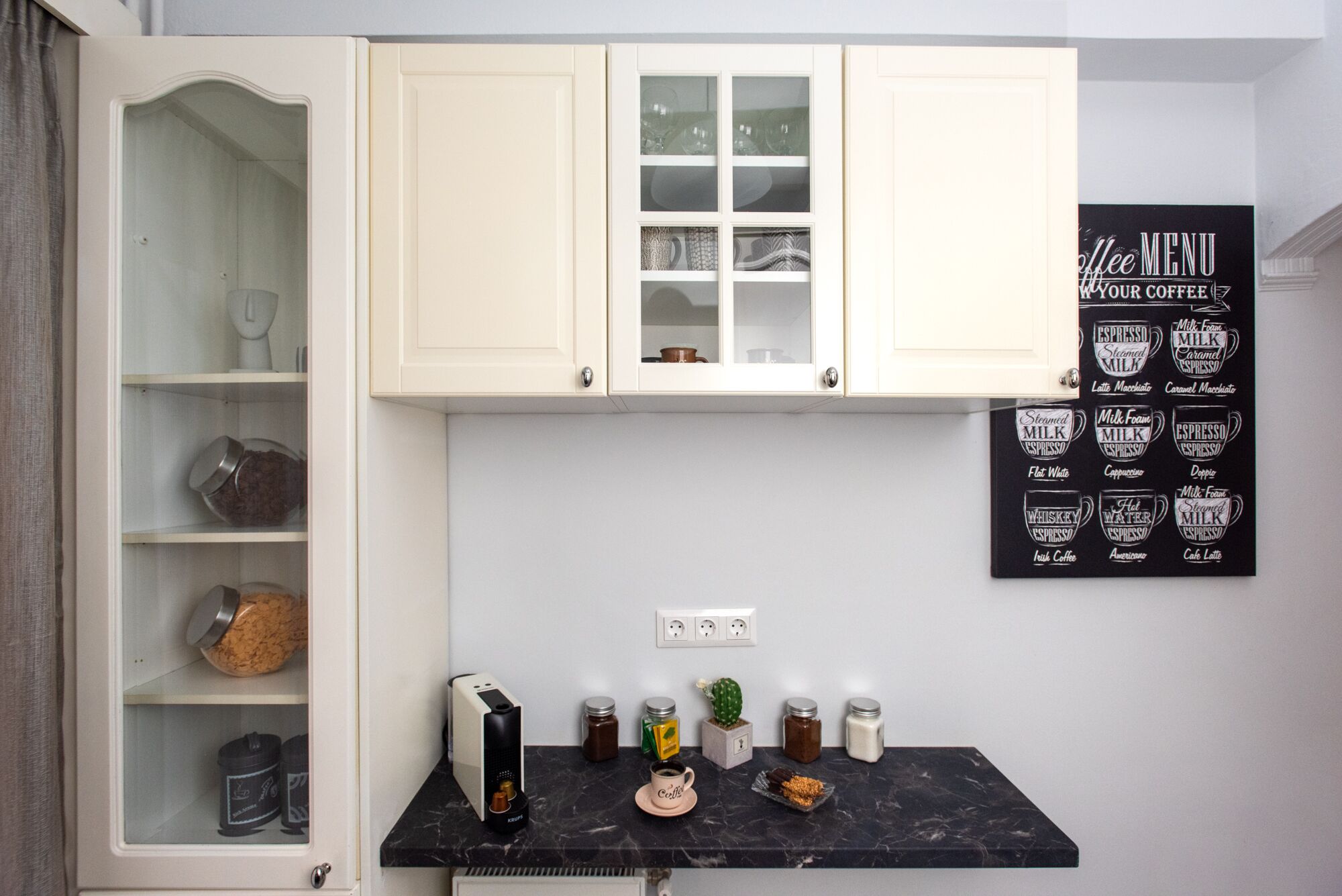 Una cocina con gabinetes blancos, encimera de mármol y zona de café.