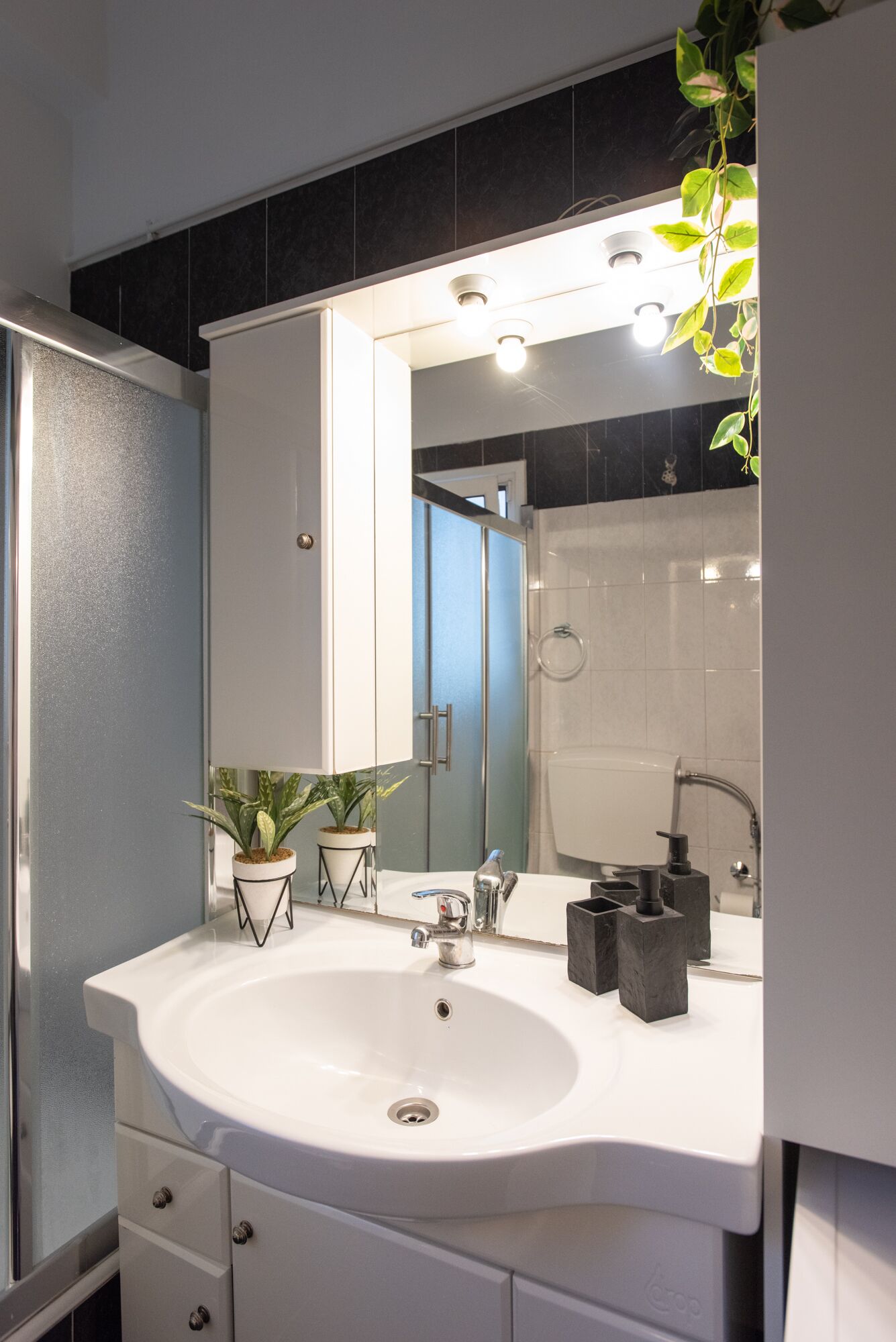 A modern bathroom with a white sink, a large mirror, and a potted plant.
