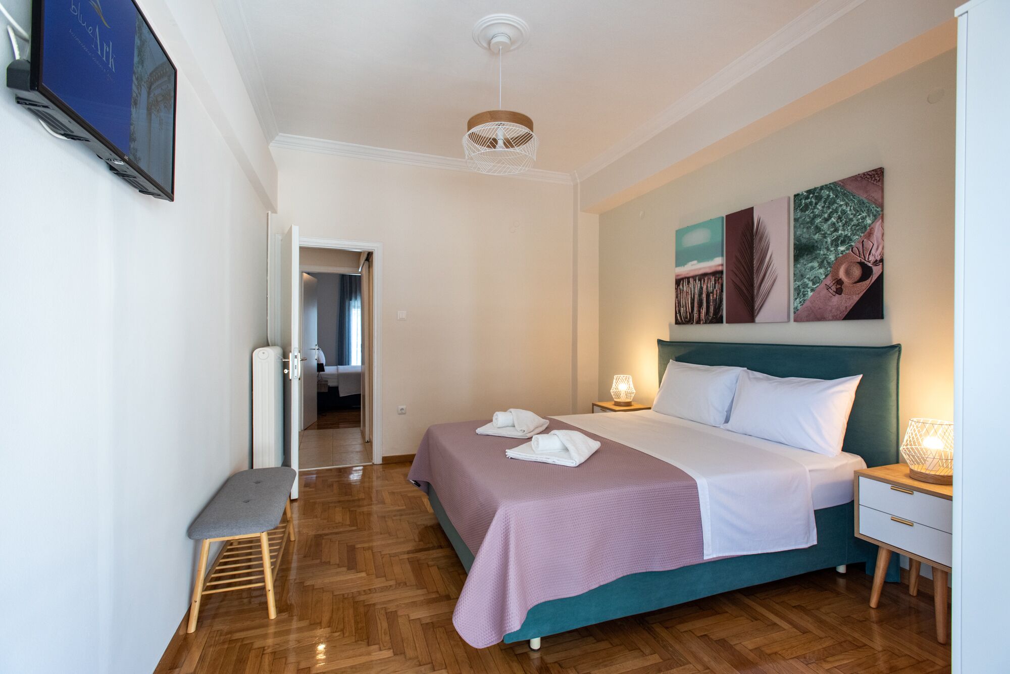 A hotel room with a bed, bedside tables, a bench, and artwork on the wall.