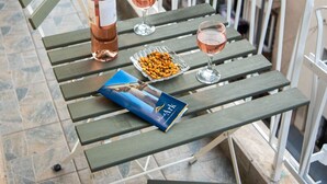 A balcony with a table set for two, featuring a bottle of rosé wine, two glasses, a small plate of nuts, and a book.