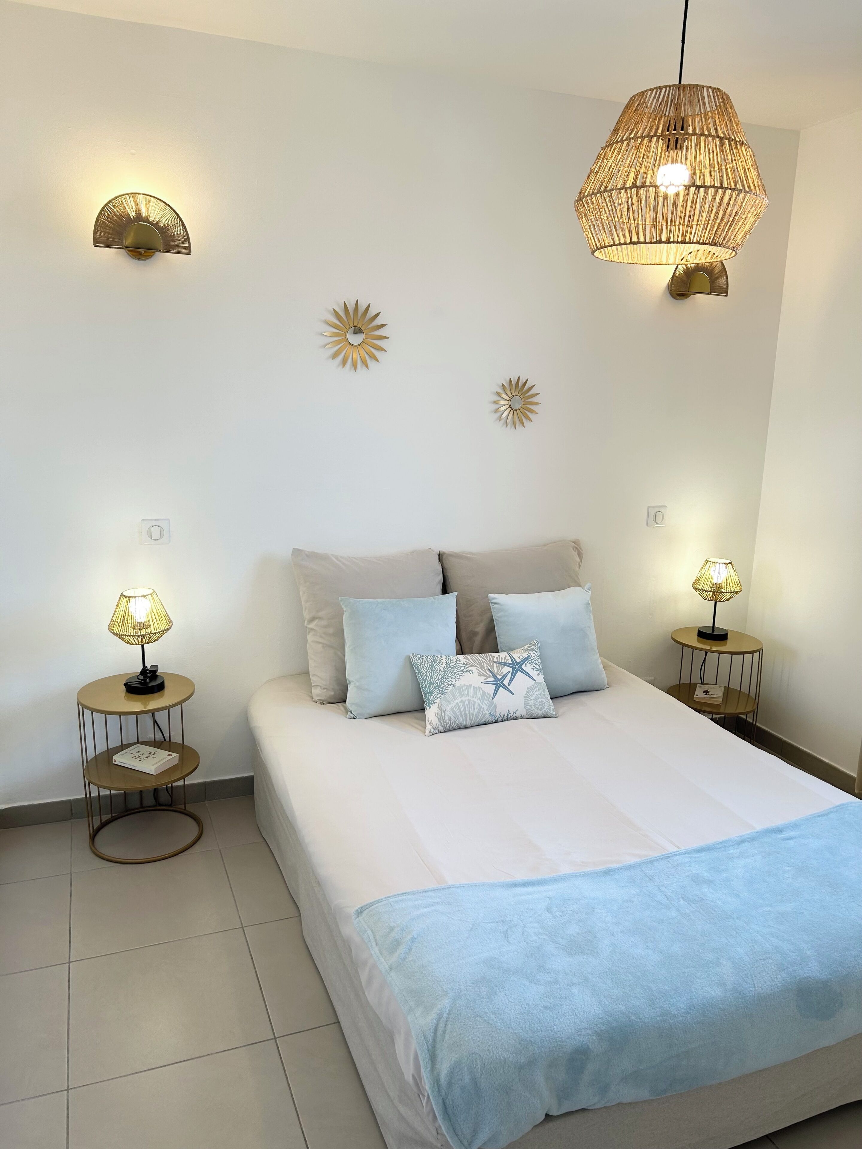 A neatly arranged bedroom with a bed, two bedside tables with lamps, and decorative wall sconces.