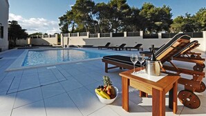 Ein Poolbereich mit Liegestühlen, einem Tisch mit Obstschale und Champagnerflasche und freiem Blick auf den Pool.