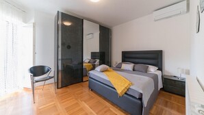 Ein modernes Schlafzimmer mit einem großen Bett, einem Sessel, einem Kleiderschrank und einem Spiegel.