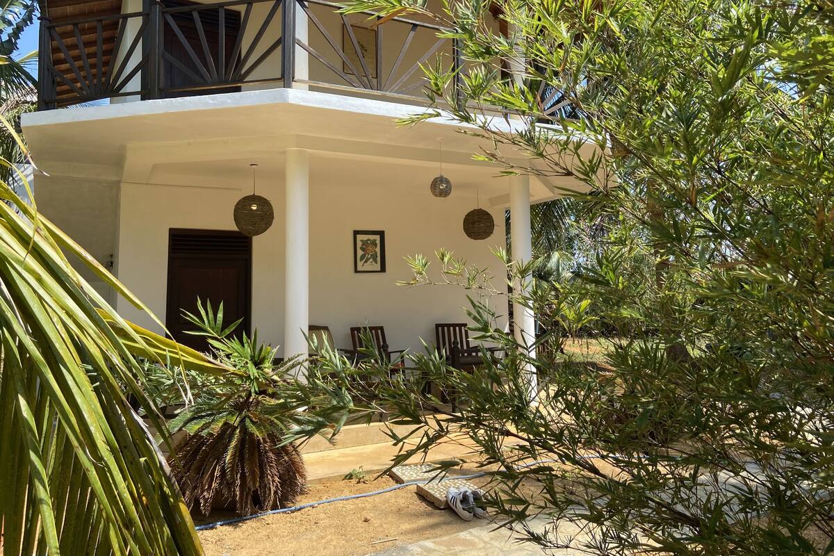 A two-story building with a balcony, outdoor seating area, and various plants.
