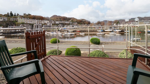 A wooden deck with two green chairs, overlooking a marina with boats and a town in the background. - Branwen (Porthmadog)
