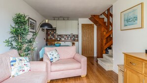 A cozy living room with a pink sofa, a wooden cabinet, and a staircase leading to a loft. - Branwen (Porthmadog)