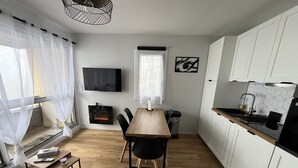 Una cocina moderna con armarios blancos, una mesa de comedor de madera y un televisor negro montado en la pared.
