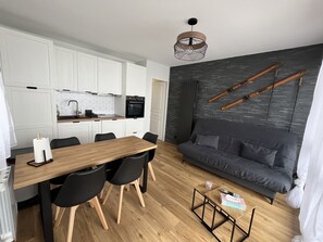 Moderni keittiö, jossa on valkoiset kaapit, puinen ruokapöytä ja harmaa sohva.