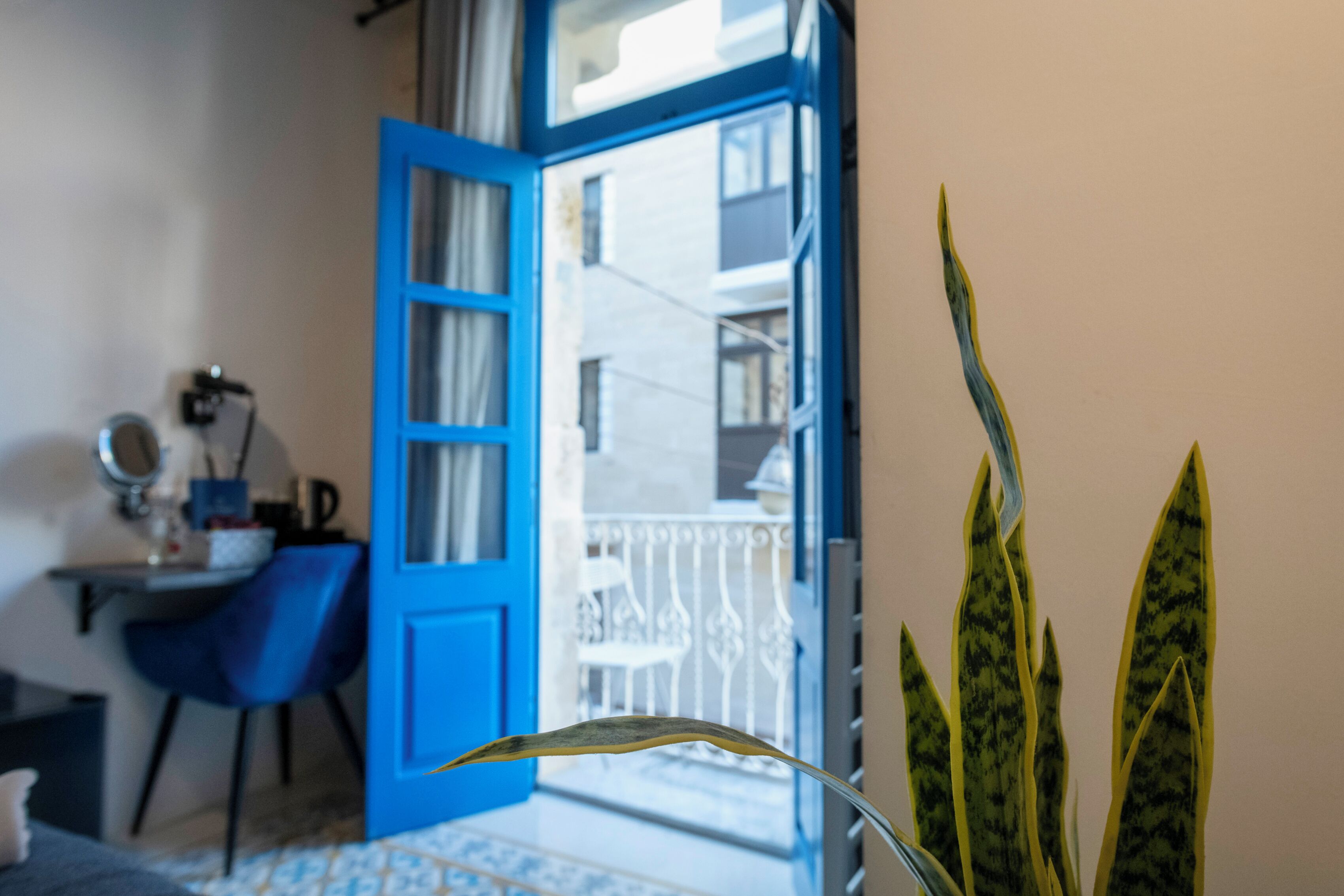 A room with a blue door leading to a balcony, a desk with a chair, and a potted plant.