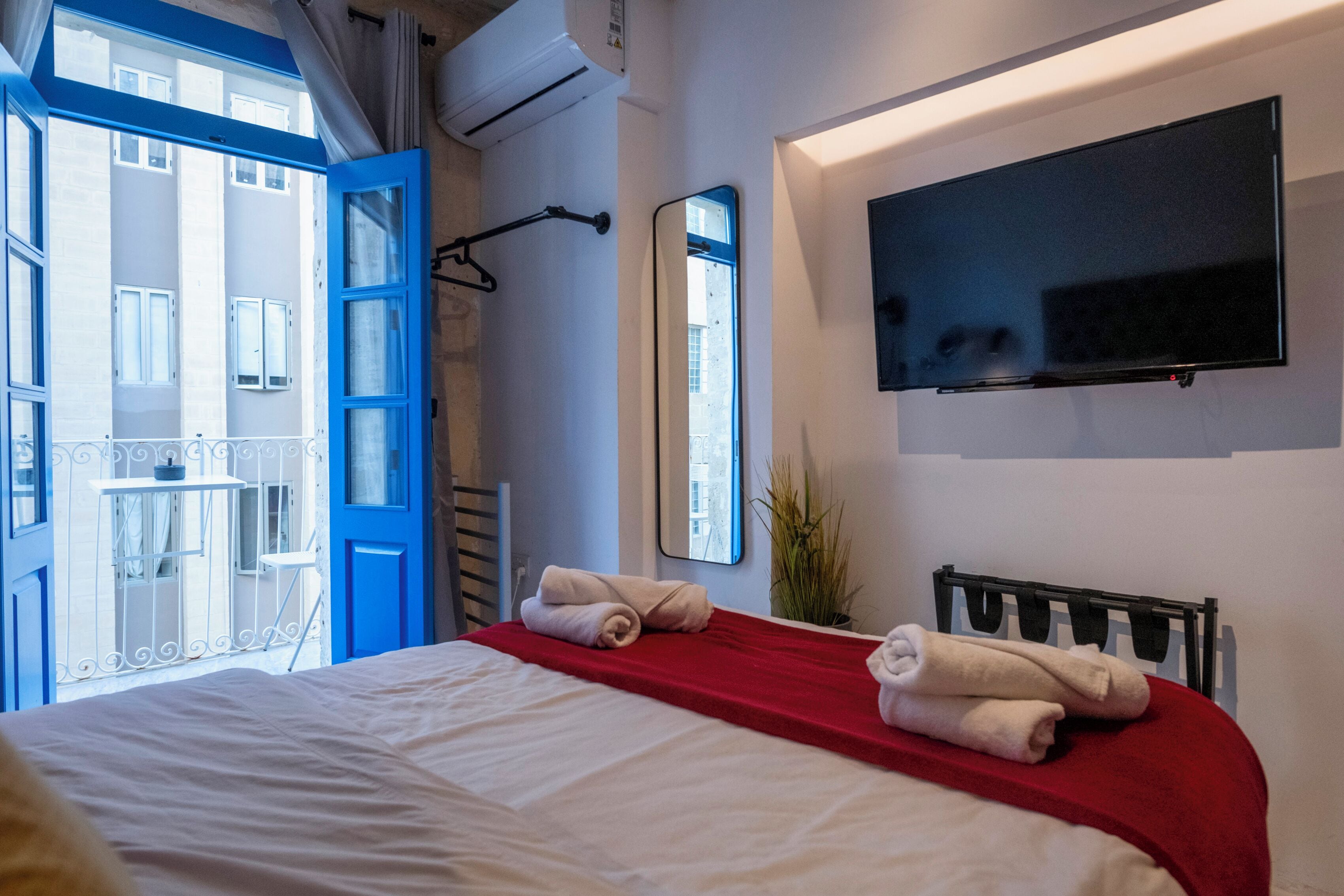 A hotel room with a bed, a TV mounted on the wall, and a balcony with blue doors.