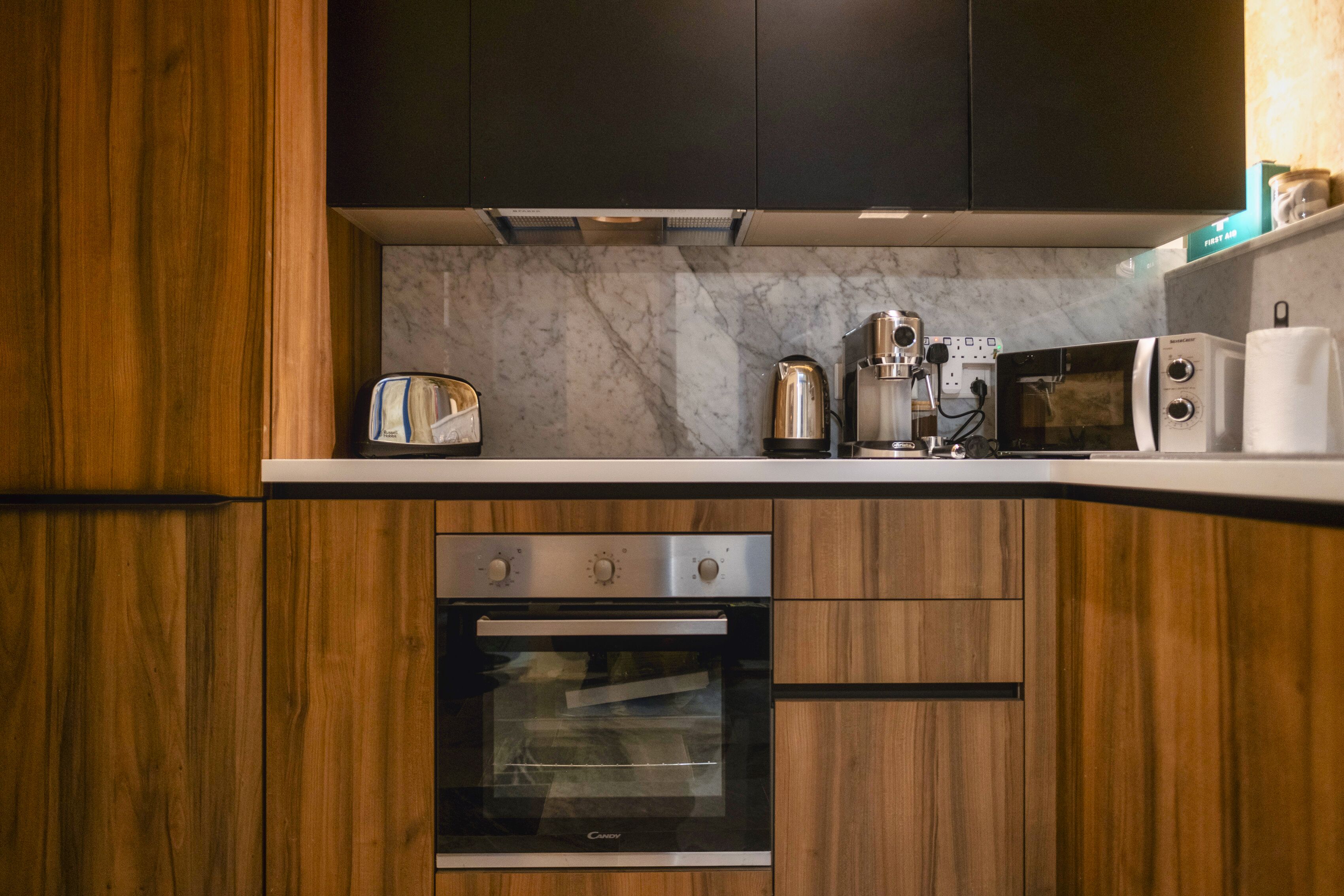 A modern kitchen with wooden cabinets, a built-in oven, a microwave, and a coffee maker.