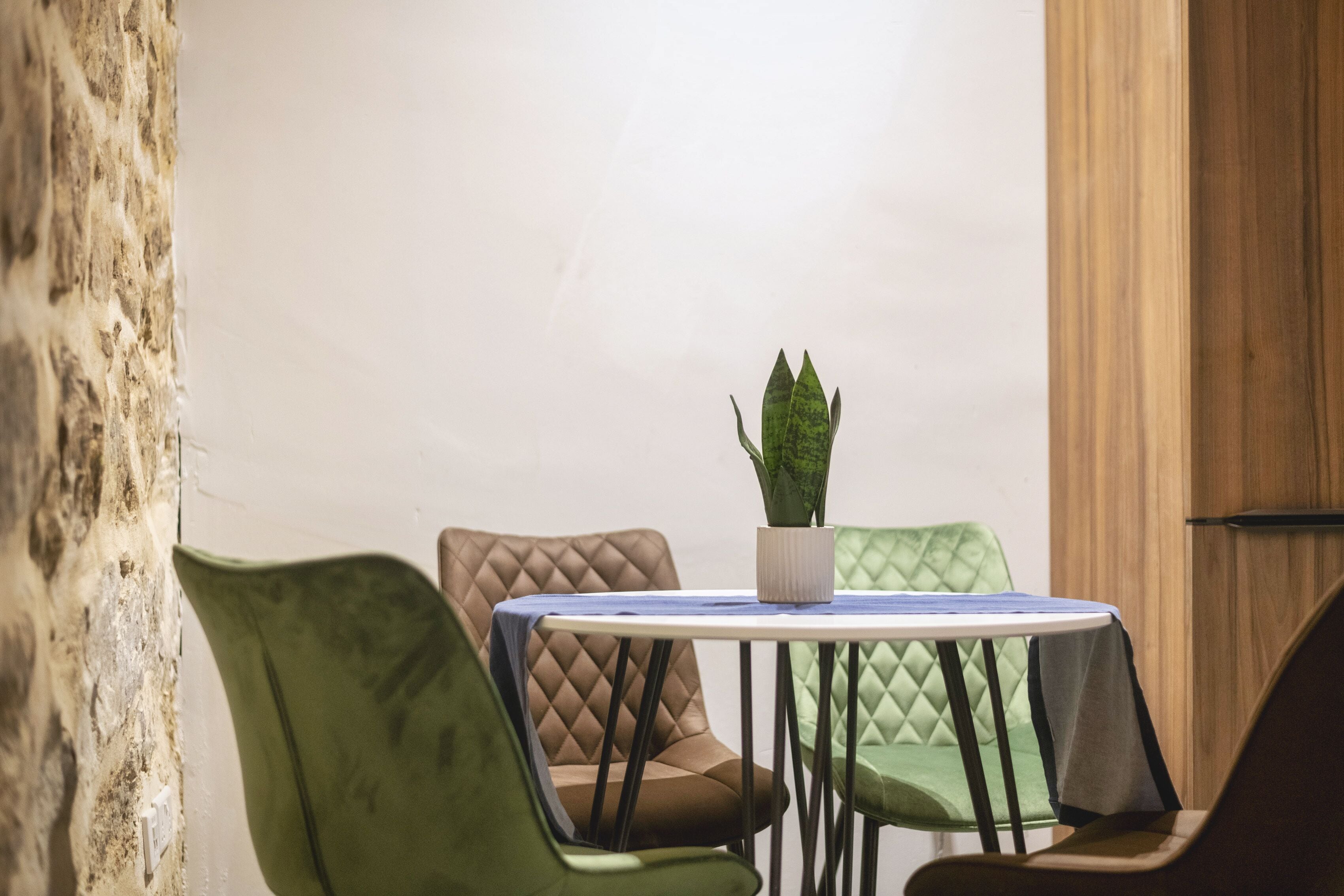 Et lille rundt bord med en potteplante, omgivet af polstrede stole med et quiltet mønster.