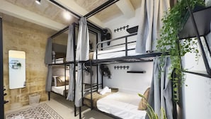Een slaapkamer met een stapelbed, een tapijt met geometrisch patroon, een spiegel en een plant.