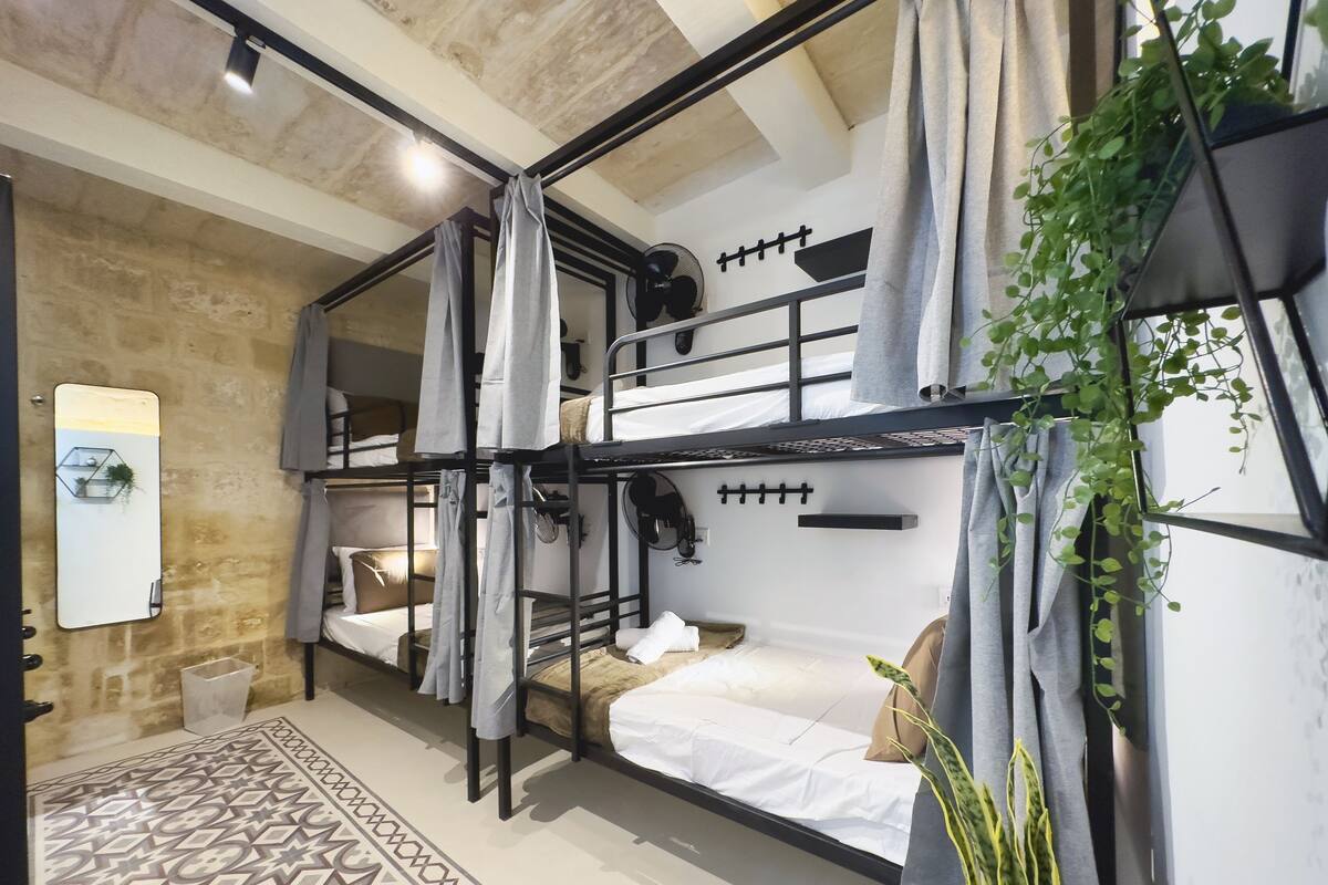 Une chambre avec un lit superposé, un tapis à motifs géométriques, un miroir et une plante.