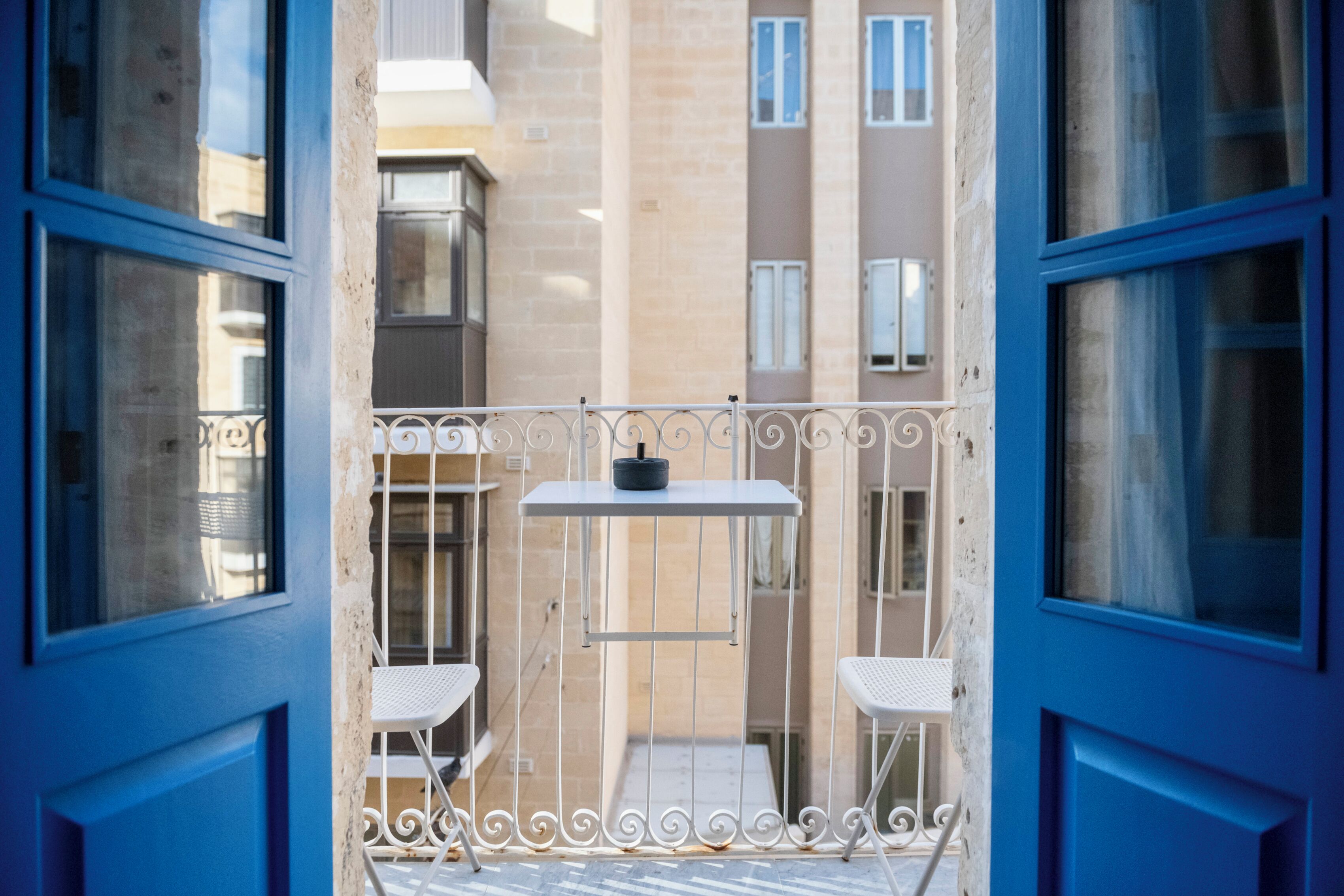 A balcony with a small table and two chairs, a metal railing, and a view of adjacent buildings.