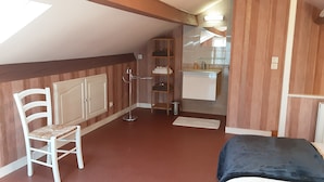 Ein kleines, gemütliches Zimmer mit einem Einzelbett, einem Sessel, einem Kleiderschrank, einer kleinen Küchenzeile und einem Heizkörper.