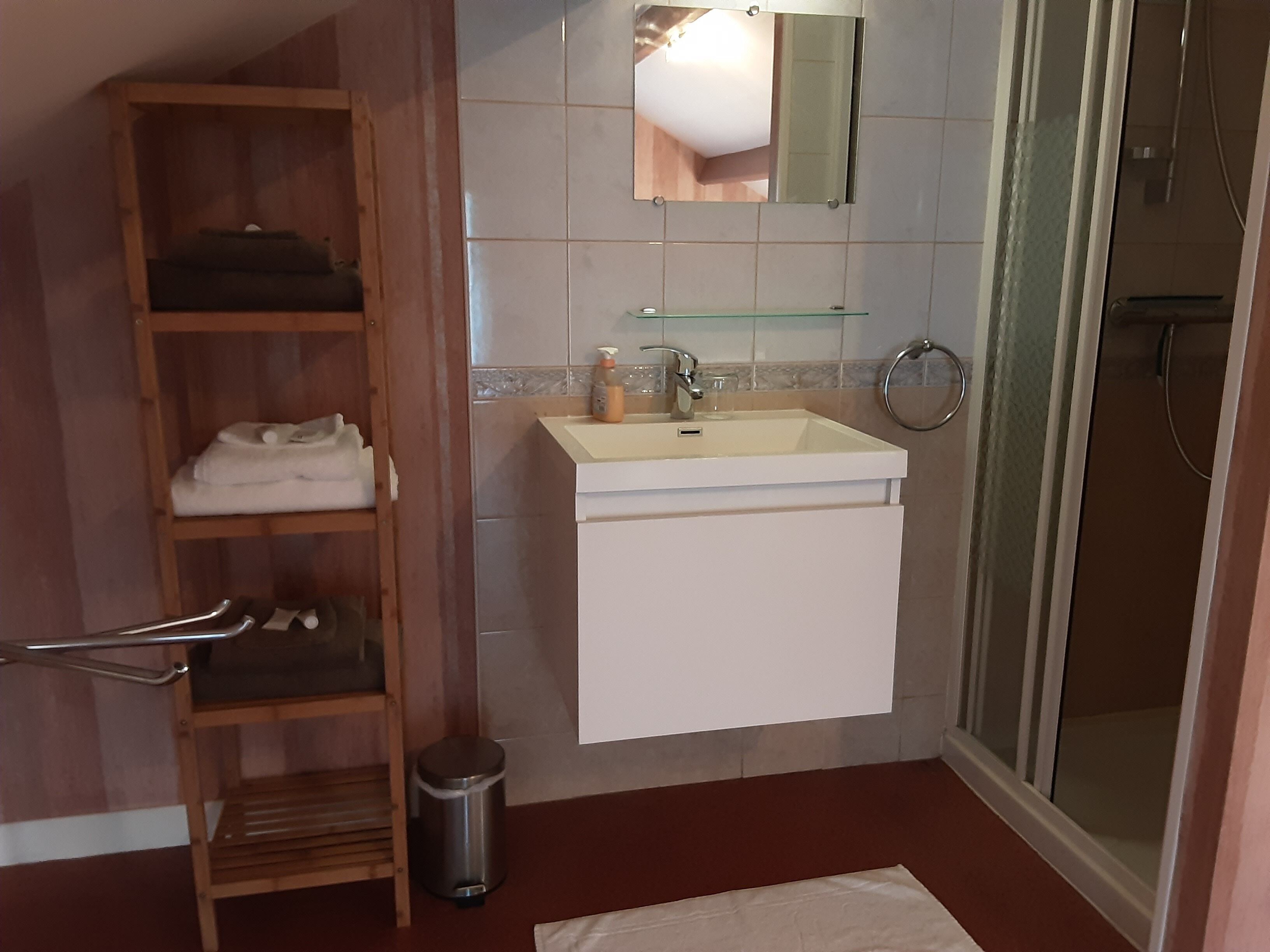 A bathroom with a wooden shelf, a white sink, a mirror, and a shower area.