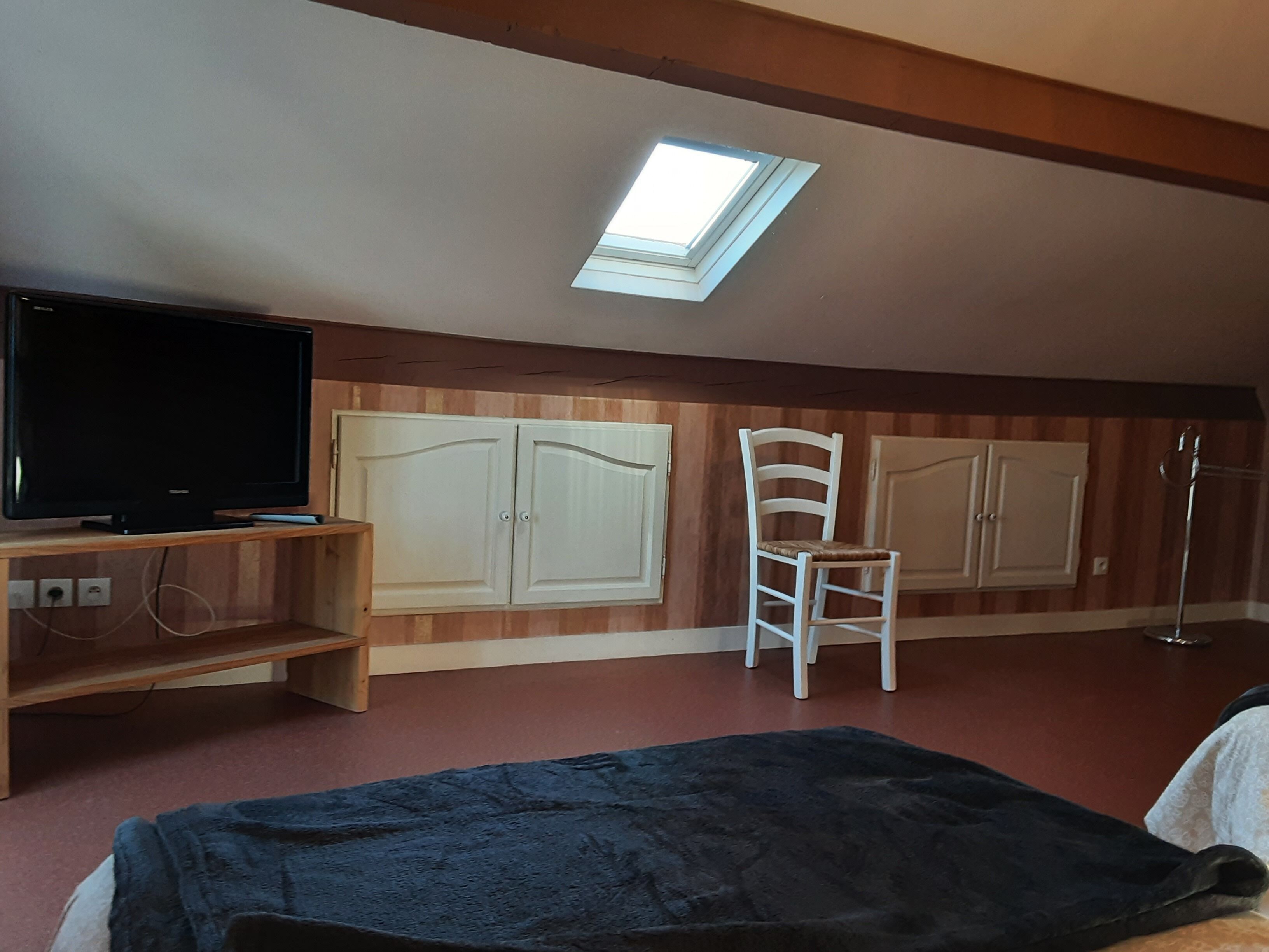 Ein Zimmer mit Fernseher auf einem Holzboden, einem weißen Stuhl, einem Kleiderschrank und einem Oberlicht.
