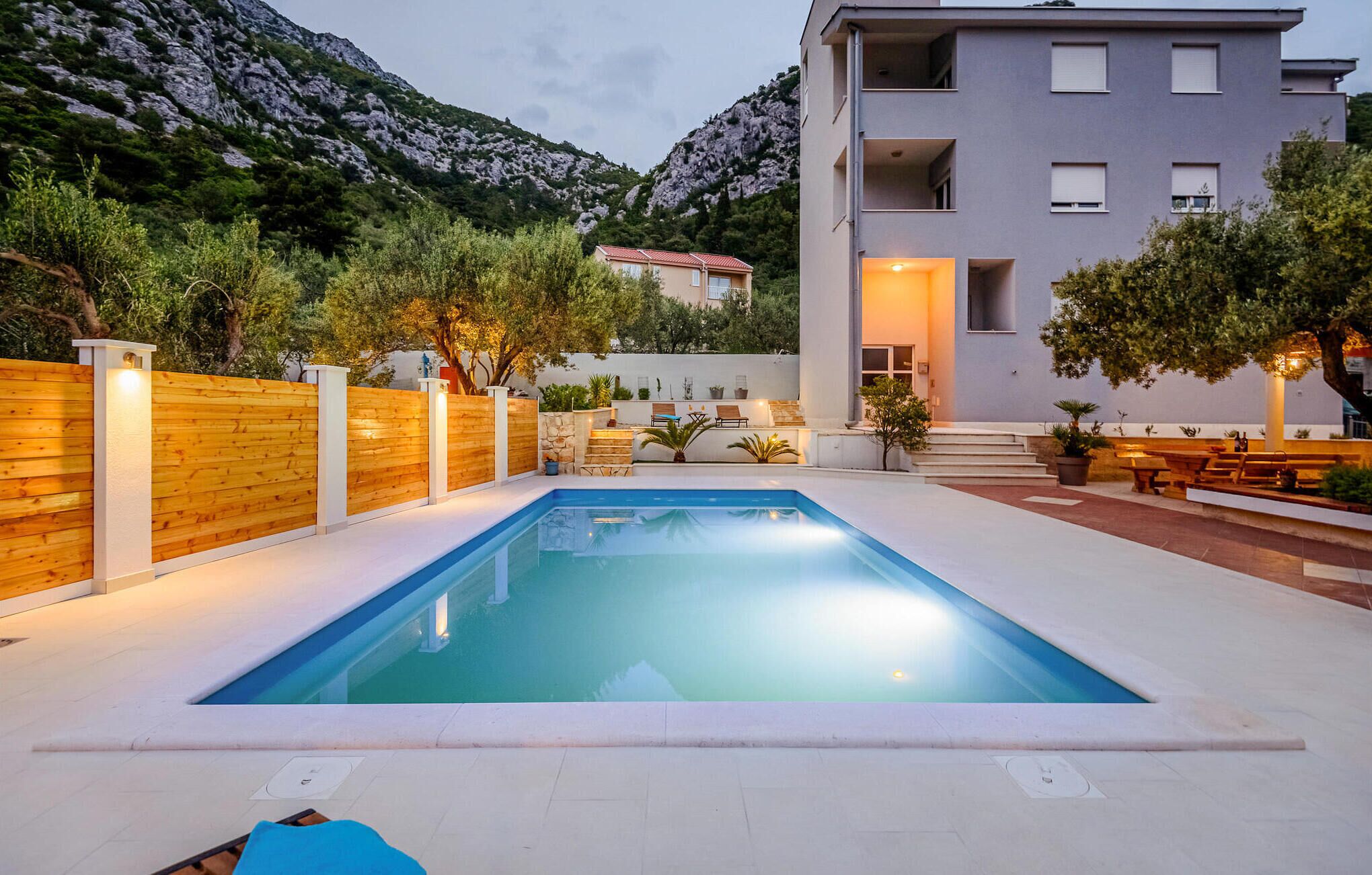 Une piscine entourée d’une clôture en bois, avec un espace extérieur aménagé et une vue sur les montagnes.