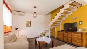 Een woonkamer met een trap, een bank, een bijzettafeltje, een televisie en een houten kast.