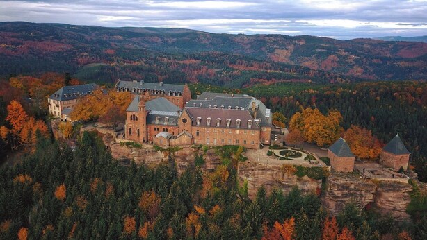 A historic building complex with multiple structures, including a church with a prominent tower, situated on a cliff overlooking a forested valley. - Climontaine Chalet with Jacuzzi - Vosges Mountains (Colroy-la-Roche)