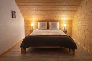 A bedroom with a wooden ceiling, a bed with a floral bedspread, two bedside lamps, and a small picture on the wall.