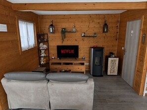 Une pièce confortable avec un canapé, un téléviseur affichant le logo « NETFLIX », un petit meuble et une étagère décorative.
