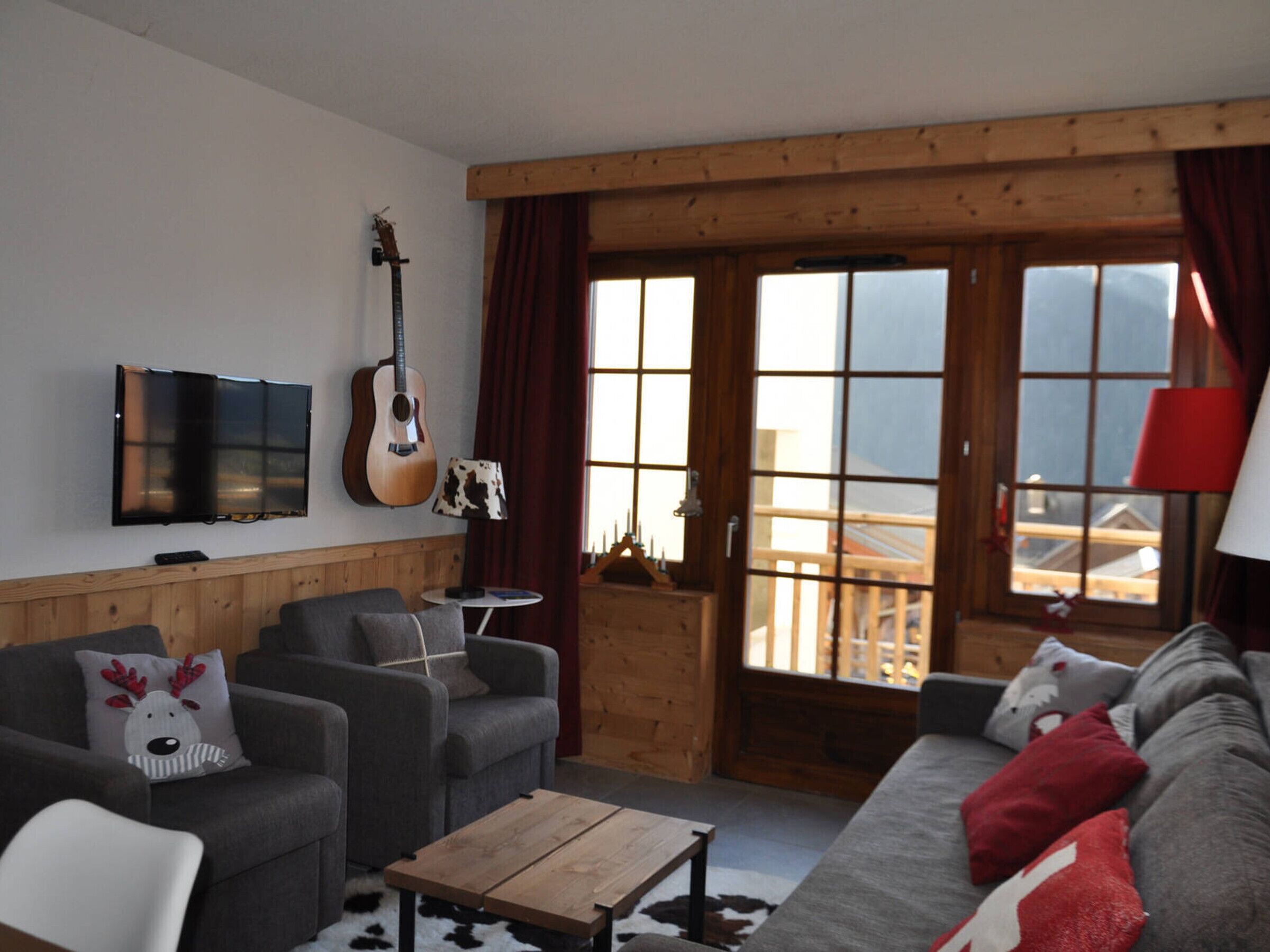 A cozy living room with a wooden ceiling, a guitar, a TV, and a sofa with reindeer pillows.