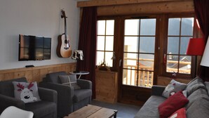 En hyggelig stue med trælofter, en guitar, et fjernsyn og en sofa med rensdyr-puder.