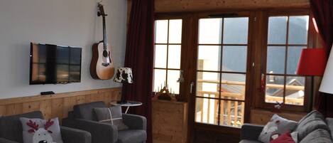 A cozy living room with a wooden ceiling, a guitar, a TV, and a sofa with reindeer pillows.