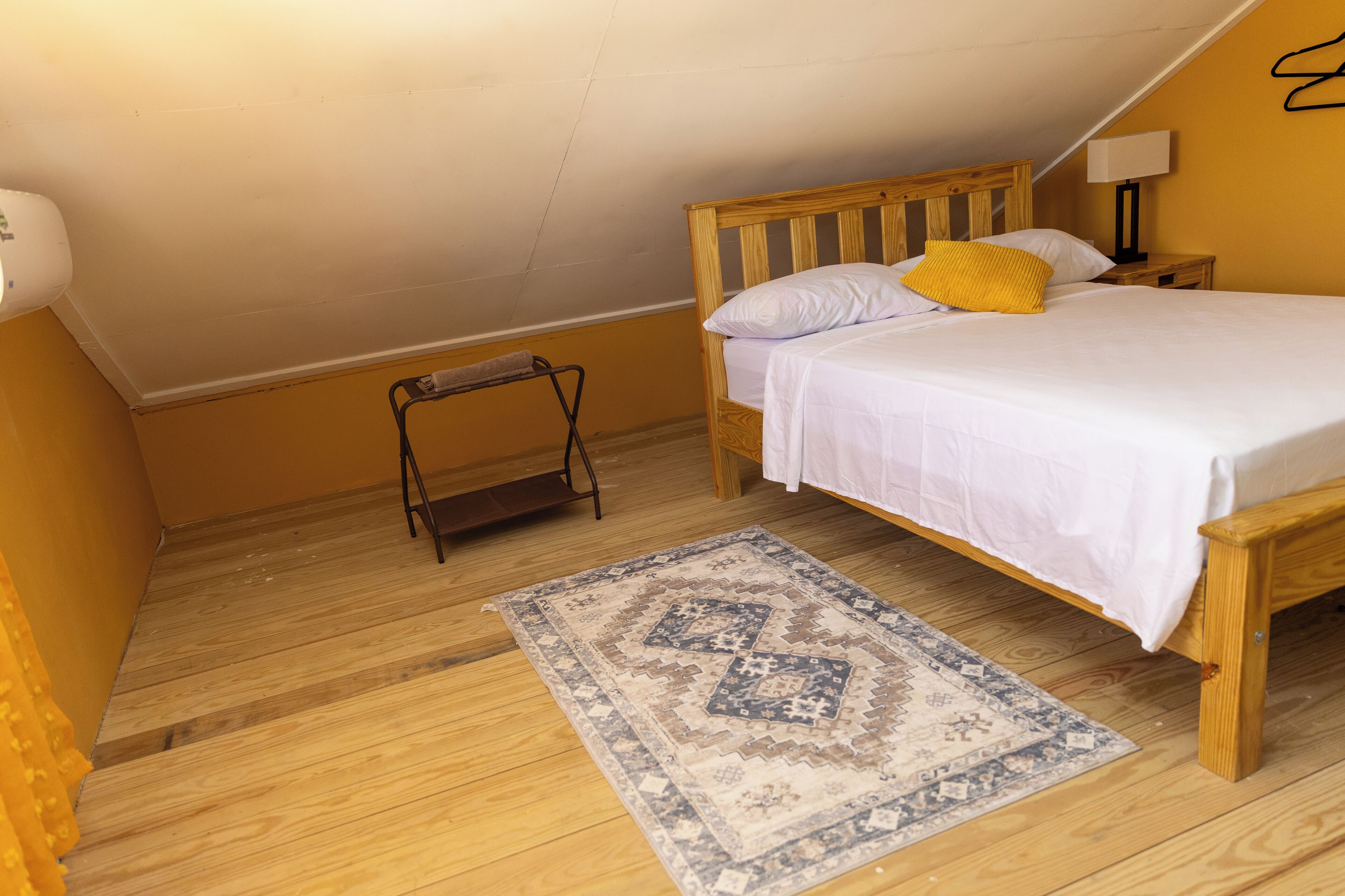 Une chambre à coucher avec un lit en bois, une table de chevet, une lampe, un petit tabouret et un tapis à motifs.
