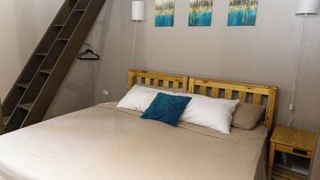 A bedroom with a bed, a wooden headboard, a nightstand, a wall-mounted lamp, and a painting.