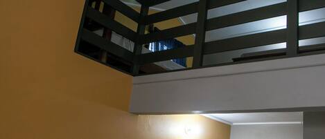 Una habitación con techo inclinado, una lámpara a la vista y un perchero con ropa.
