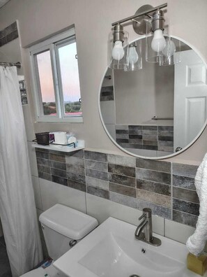 A bathroom with a toilet, sink, and a mirror with lights. - Comfi Spaces (Canaan)