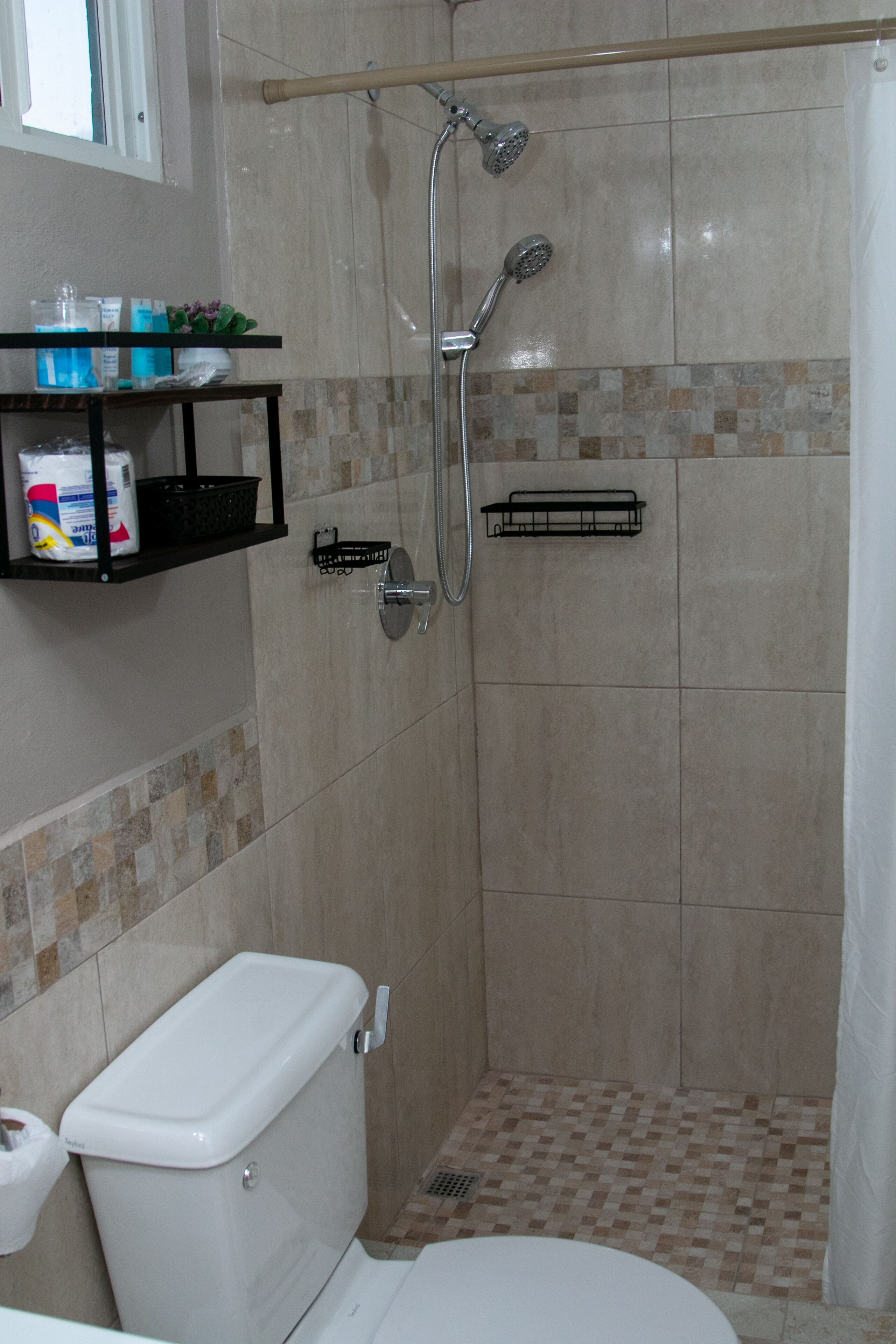 A shower area with a tiled floor, a toilet, and a shelf with toiletries.