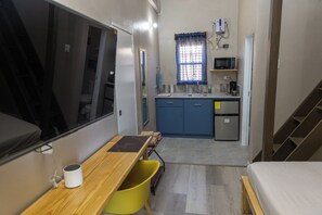 A compact room with a bed, a desk with a chair, a small kitchenette, and a bathroom. - Comfi Spaces (Canaan)