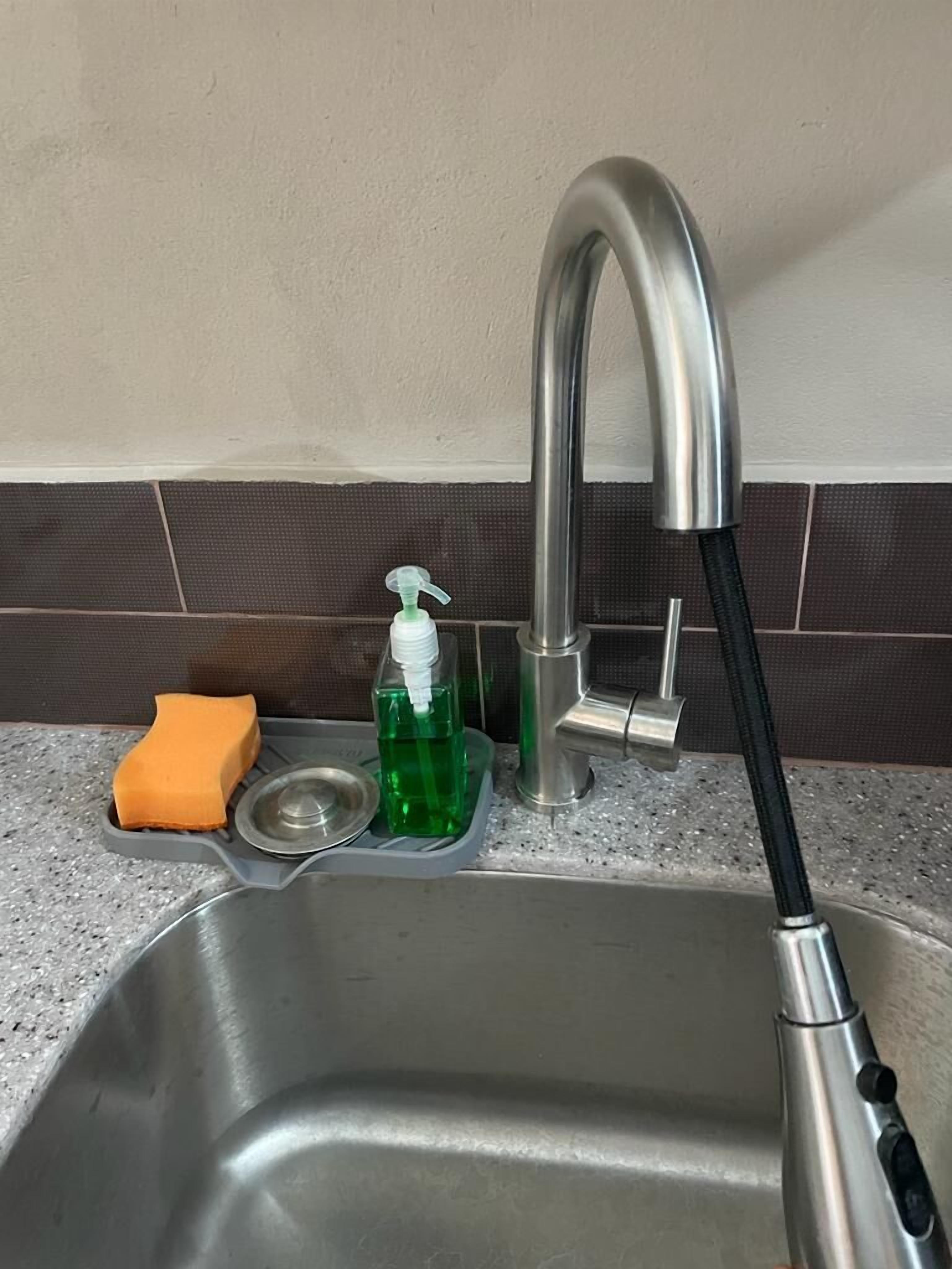 A stainless steel kitchen sink with a modern faucet, a soap dispenser, and a sponge.