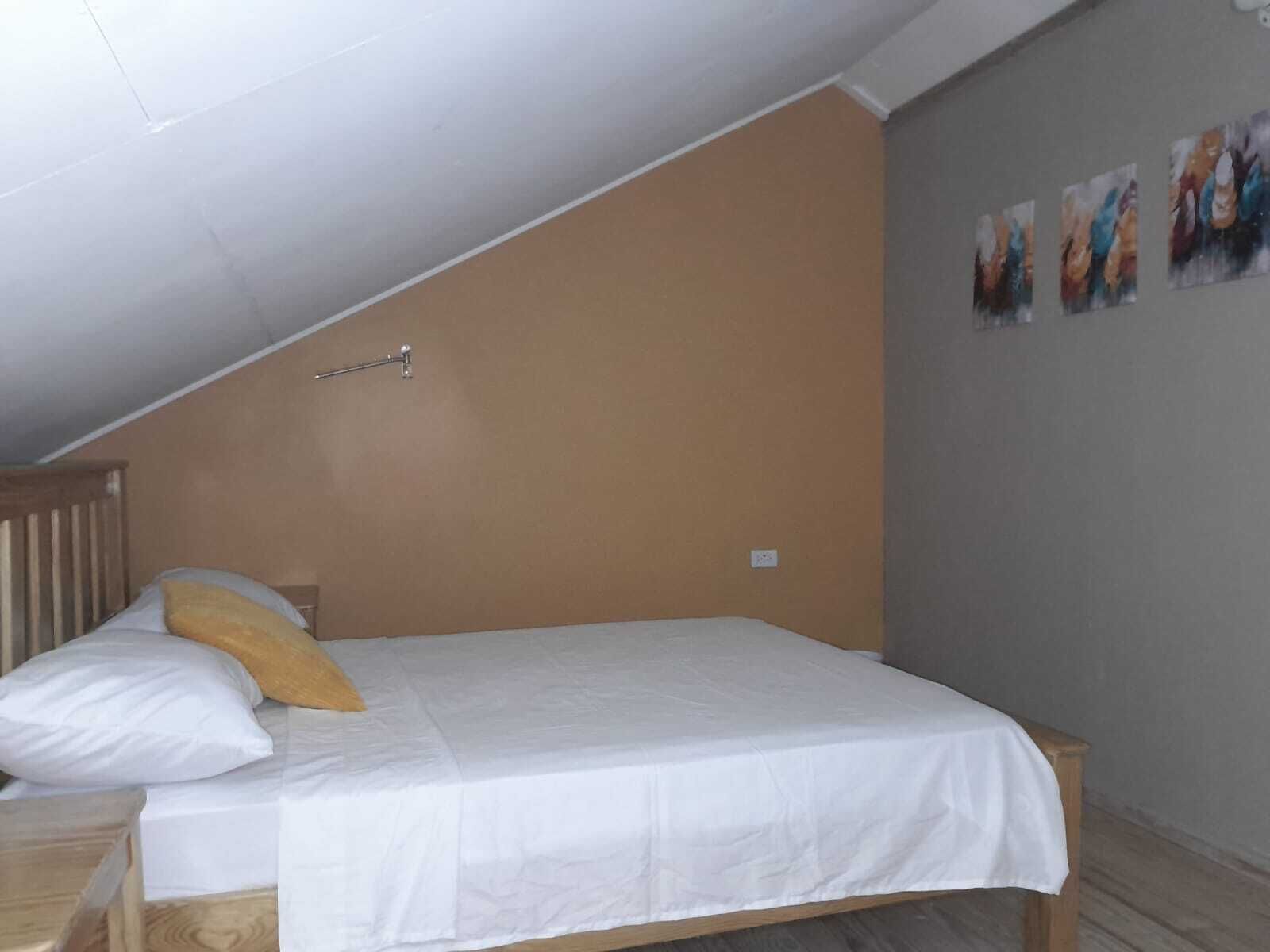 Un dormitorio con techo inclinado, una cama con ropa de cama blanca, un cabecero de madera y una pared con tres cuadros.