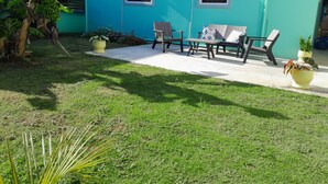 Un bâtiment de couleur turquoise avec deux fenêtres, une terrasse dotée de mobilier d’extérieur et de plantes en pot.