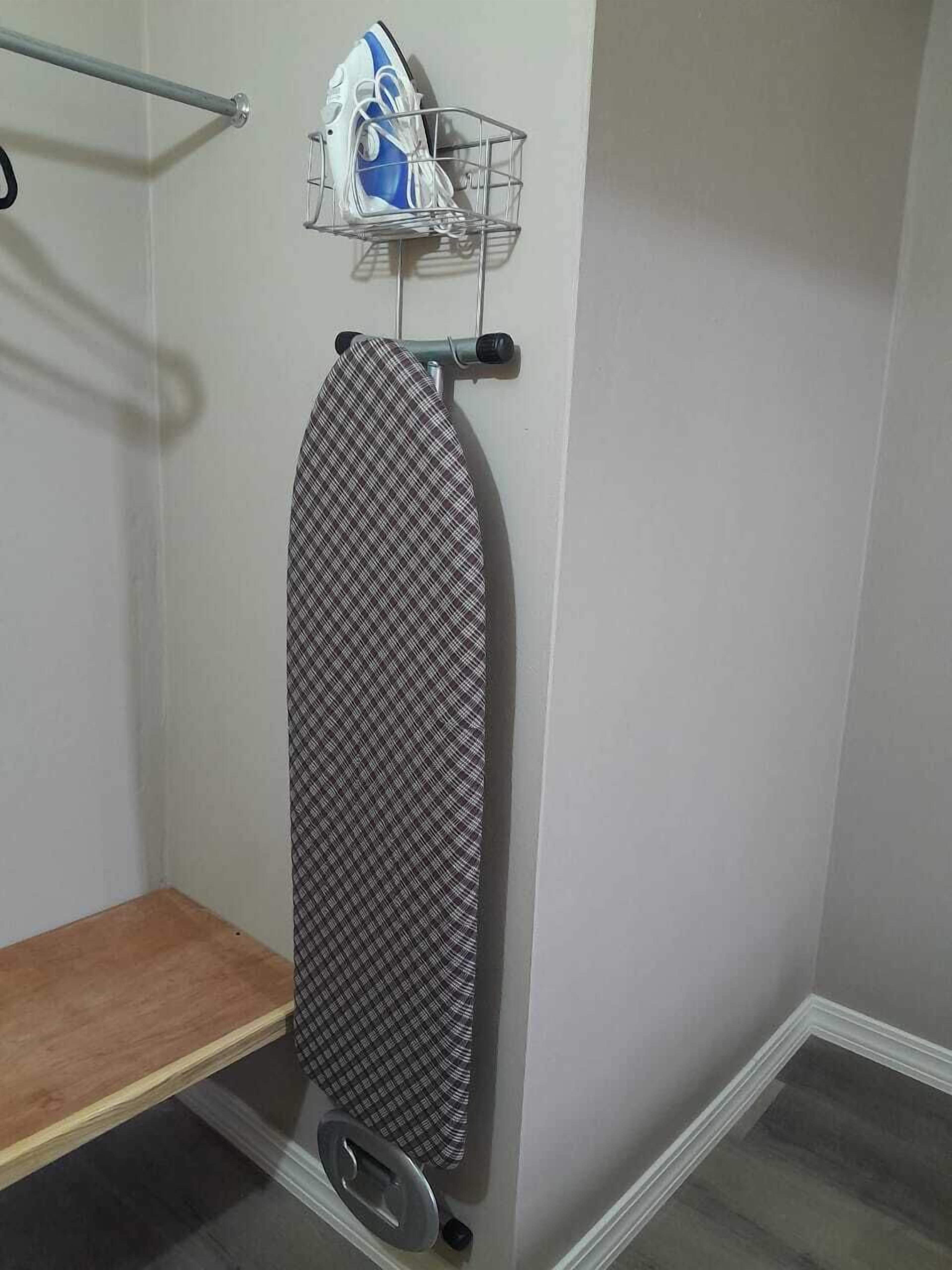 A corner of a room with a wooden shelf, an ironing board, and a metal rack holding a blue and white iron.
