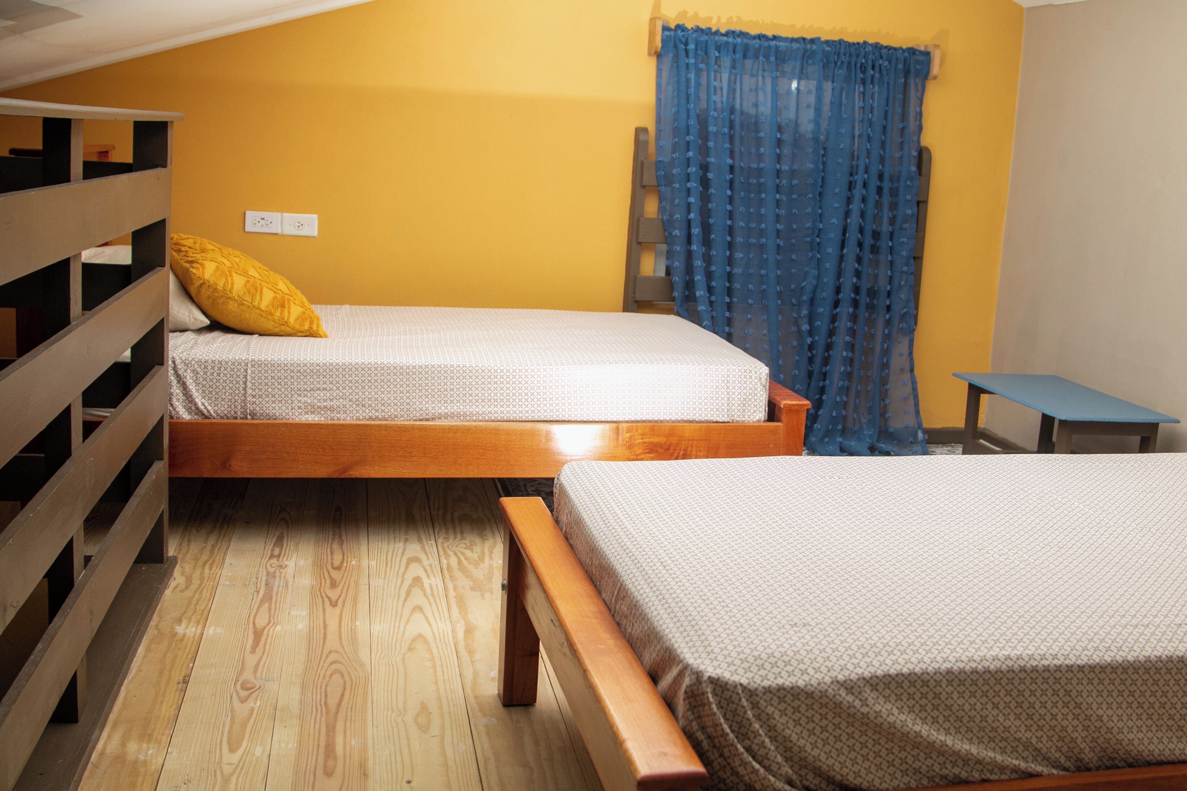 A room with two wooden bunk beds, a small table, and a blue curtain.
