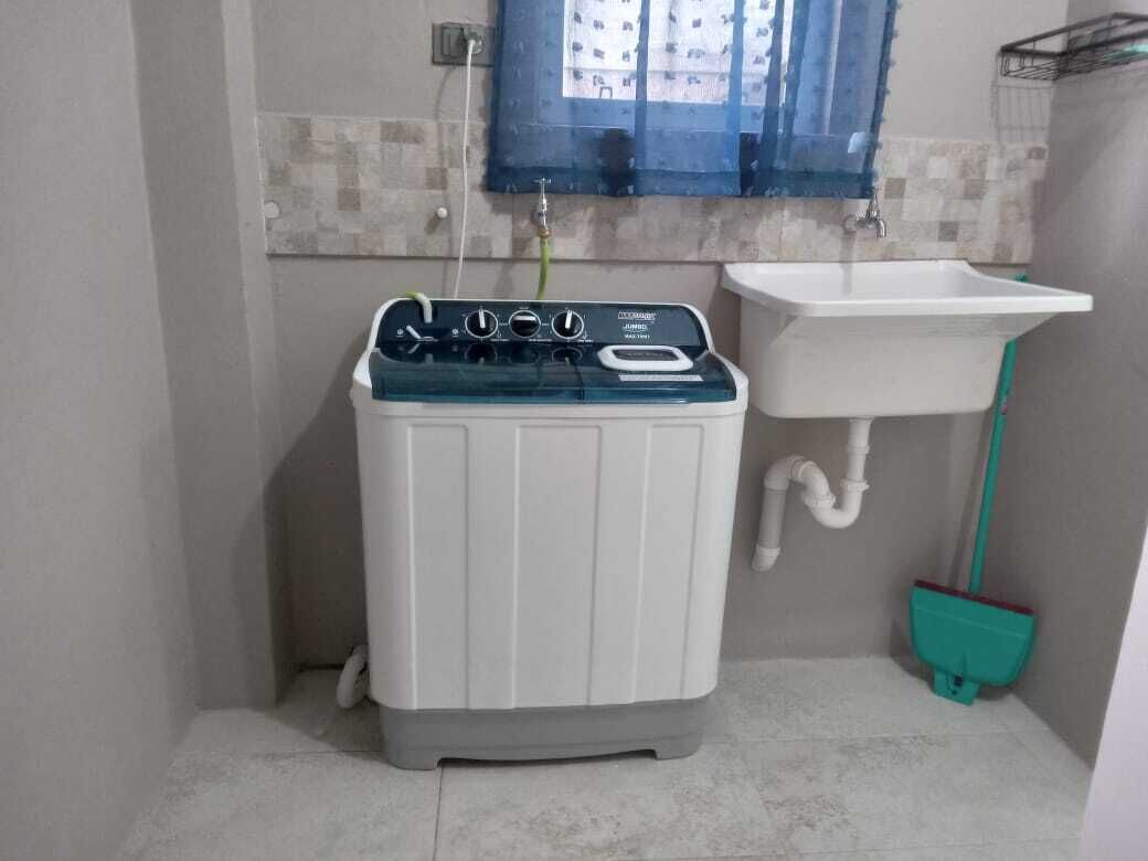 A compact laundry room with a washing machine, a sink, and a broom.