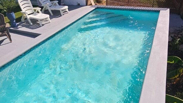 Une piscine rectangulaire à l’eau d’un bleu cristallin, entourée d’une terrasse blanche et de chaises longues blanches.